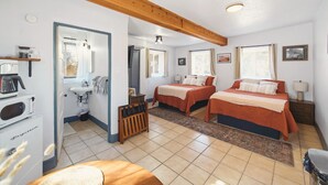 Una habitación de hotel compacta con dos camas, kitchenette, baño y una pequeña zona de estar.