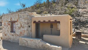 Un pequeño edificio de piedra con una ventana y una puerta, rodeado de vegetación seca.