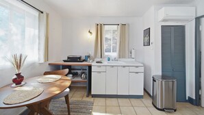 Una cocina compacta con comedor, una ventana con cortinas, un lavamanos, armarios y un cubo de basura.