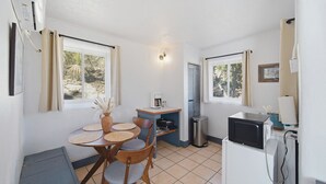 A compact kitchen with a dining table, chairs, a microwave, and a small trash bin.