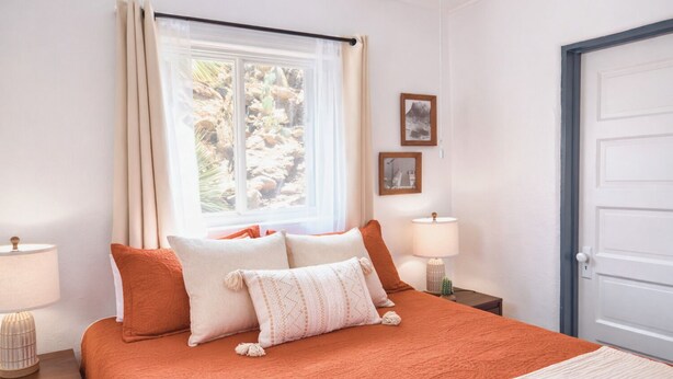 A bedroom with a bed, two bedside tables, a window with curtains, and a door.