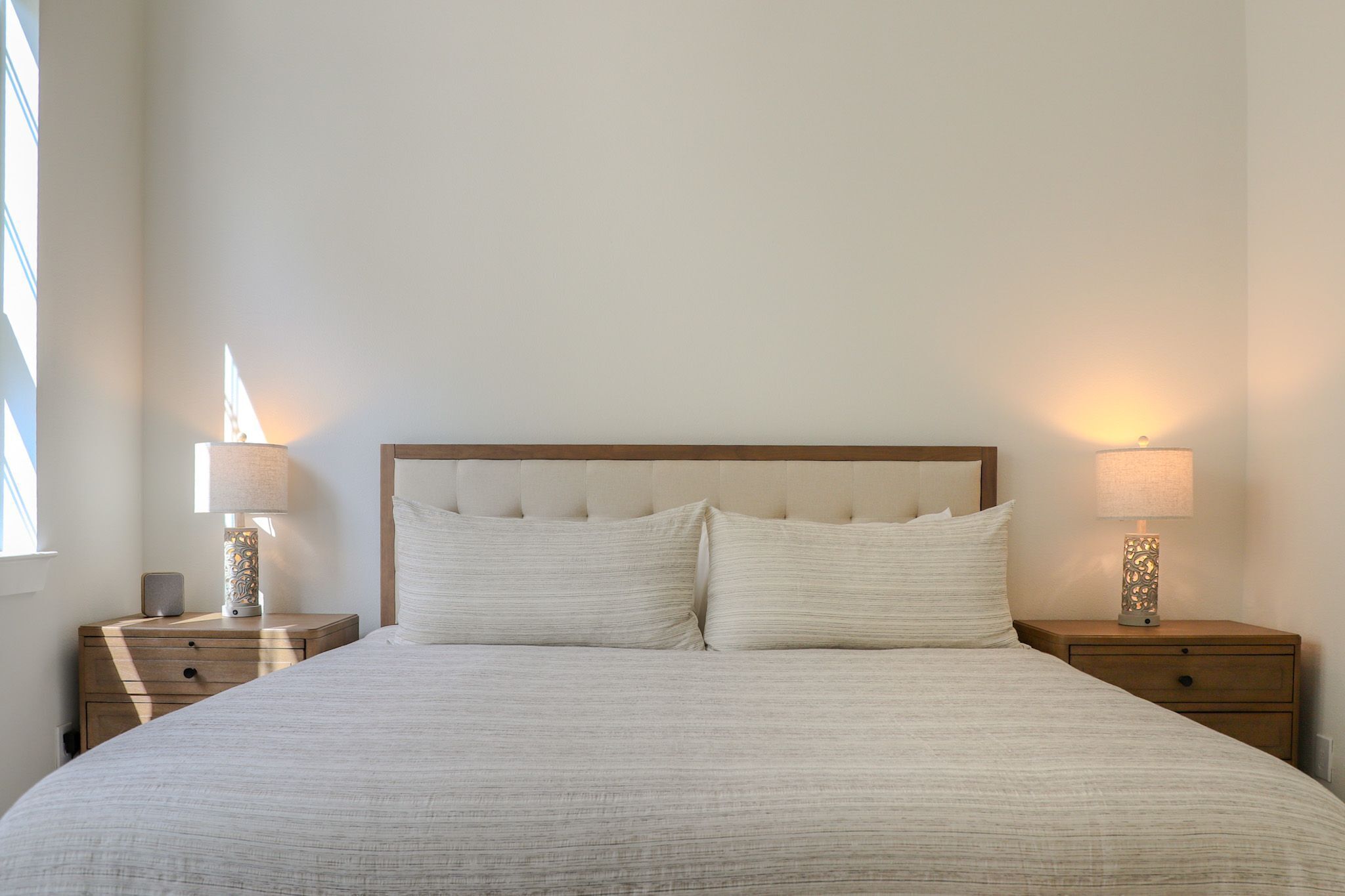 A neatly made bed with a wooden headboard, two bedside tables with lamps, and a window providing natural light.
