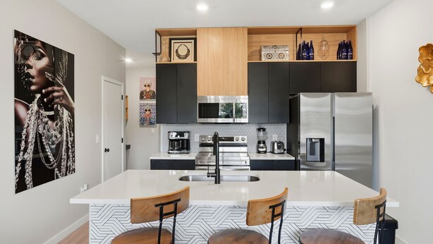A modern kitchen with a central island, stainless steel appliances, and a wooden upper shelf. - Family townhouse w/ pool & workspace (Kissimmee)