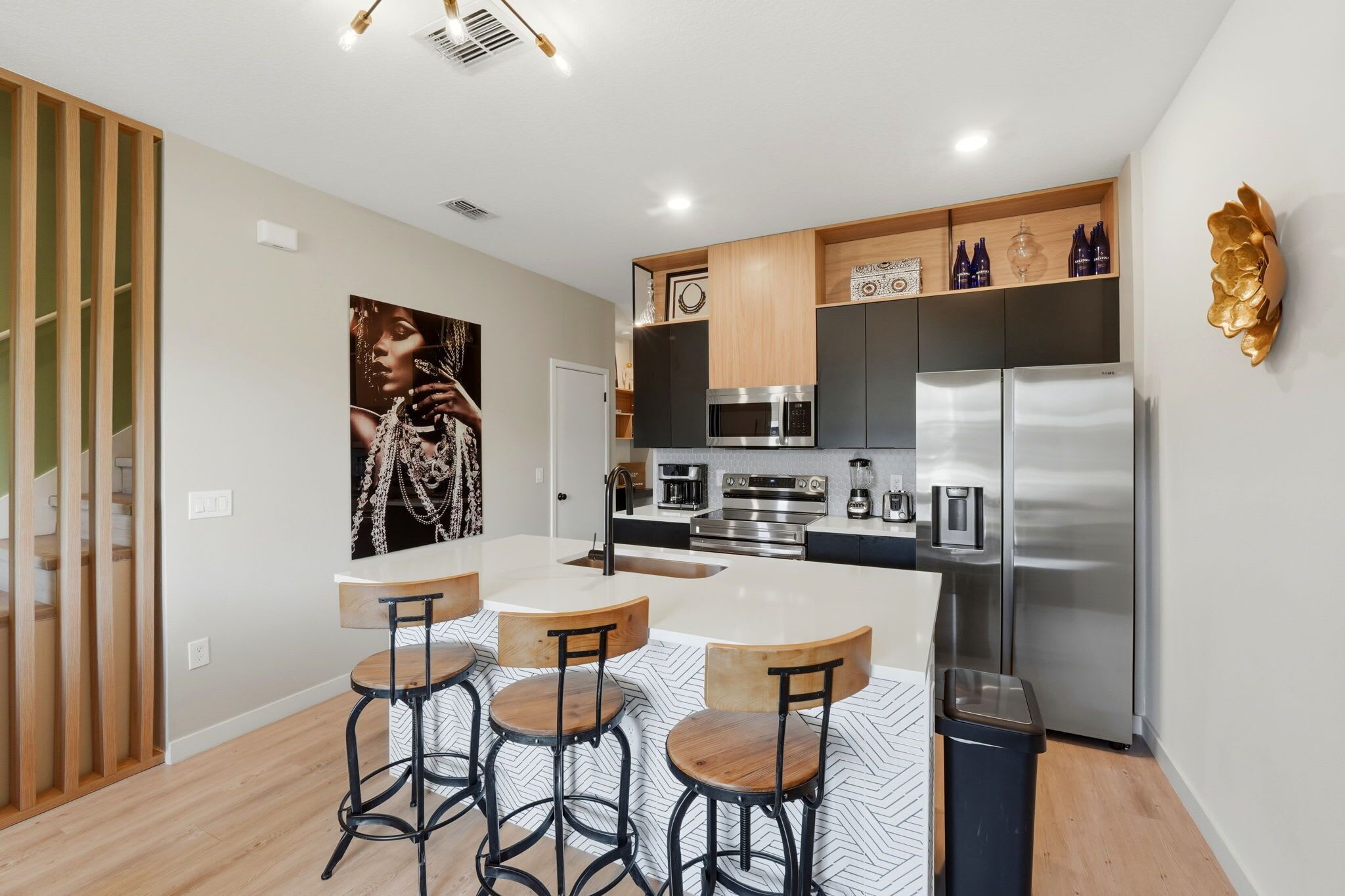 A modern kitchen with a central island, bar stools, stainless steel appliances, and a decorative wall piece.