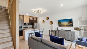 A modern kitchen with a central island, a dining area with a sofa and chairs, and a staircase leading to another level. - Family townhouse w/ pool & workspace (Kissimmee)