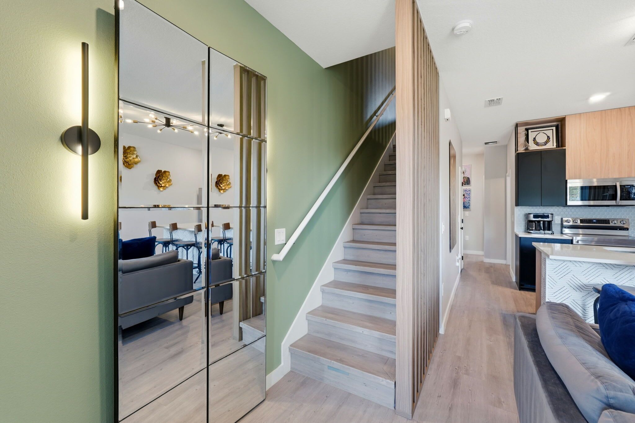 Een modern interieur met een trap die leidt naar een keuken, een woonkamer met een bank en een spiegelwand die de ruimte weerspiegelt.