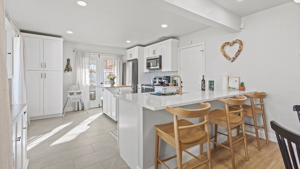 A modern kitchen with white cabinetry, a central island with bar stools, a microwave, and a heart-shaped decoration on the wall.