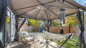 A covered patio area with a hammock, a chair, and a small table with a plant.