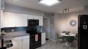 Een moderne keuken met witte kasten, een zwarte kookplaat en een magnetron. Er is een eethoek met een ronde tafel en stoelen.