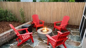 Een terras met vier rode Adirondack-stoelen rond een rond vuurkuip van natuursteen.