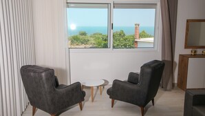 A room with two armchairs, a small round table, a large window with a view of the sea, and a wooden cabinet with a mirror. - Wake Up to Lake Views – Cozy Comfort at Era e Liqenit” (Shkodër)