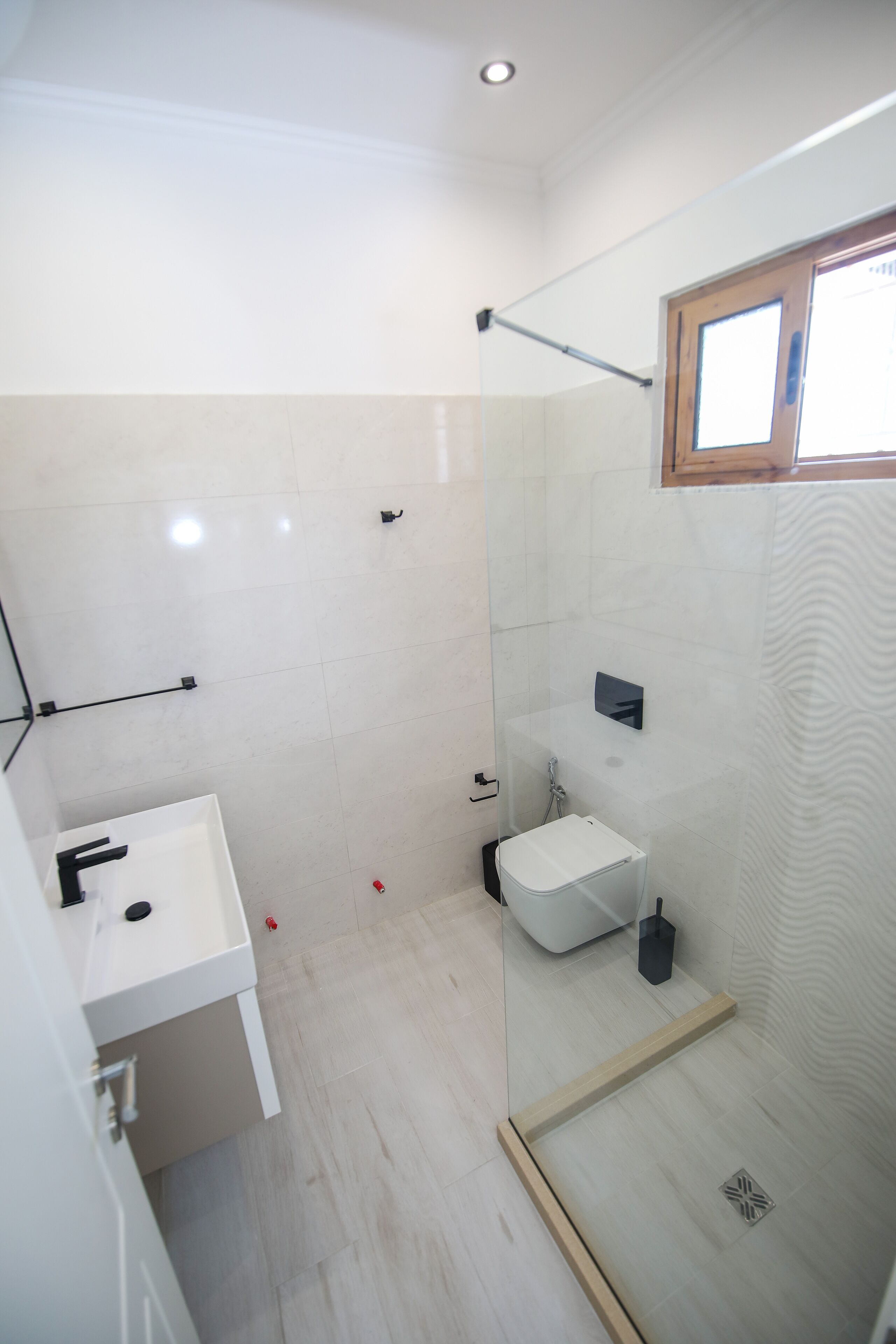 A modern bathroom with a glass shower enclosure, a white sink, and a small window.