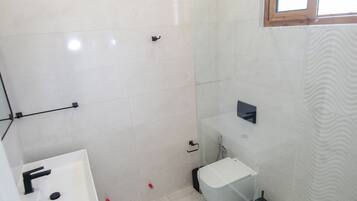 A modern bathroom with a glass shower enclosure, a white sink, and a small window.