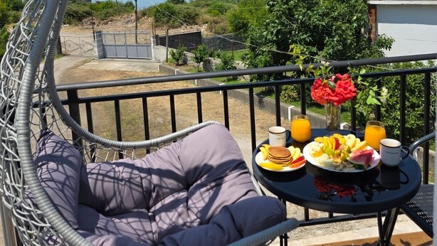 A balcony with a hanging chair, a table with breakfast, and a view of the sea and mountains. - Wake Up to Lake Views – Cozy Comfort at Era e Liqenit” (Shkodër)