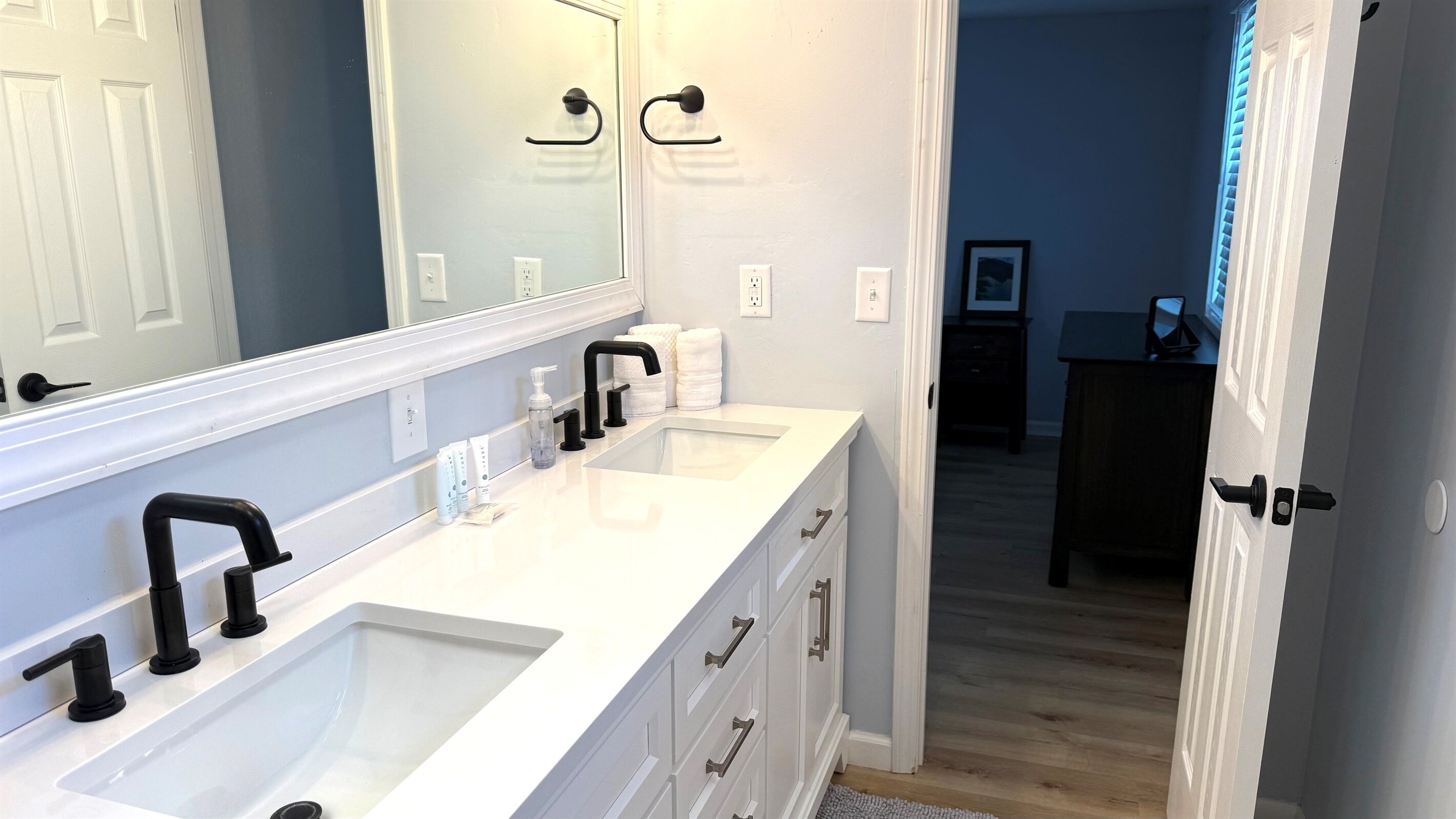 A bathroom with two sinks, a mirror, and a door leading to another room.