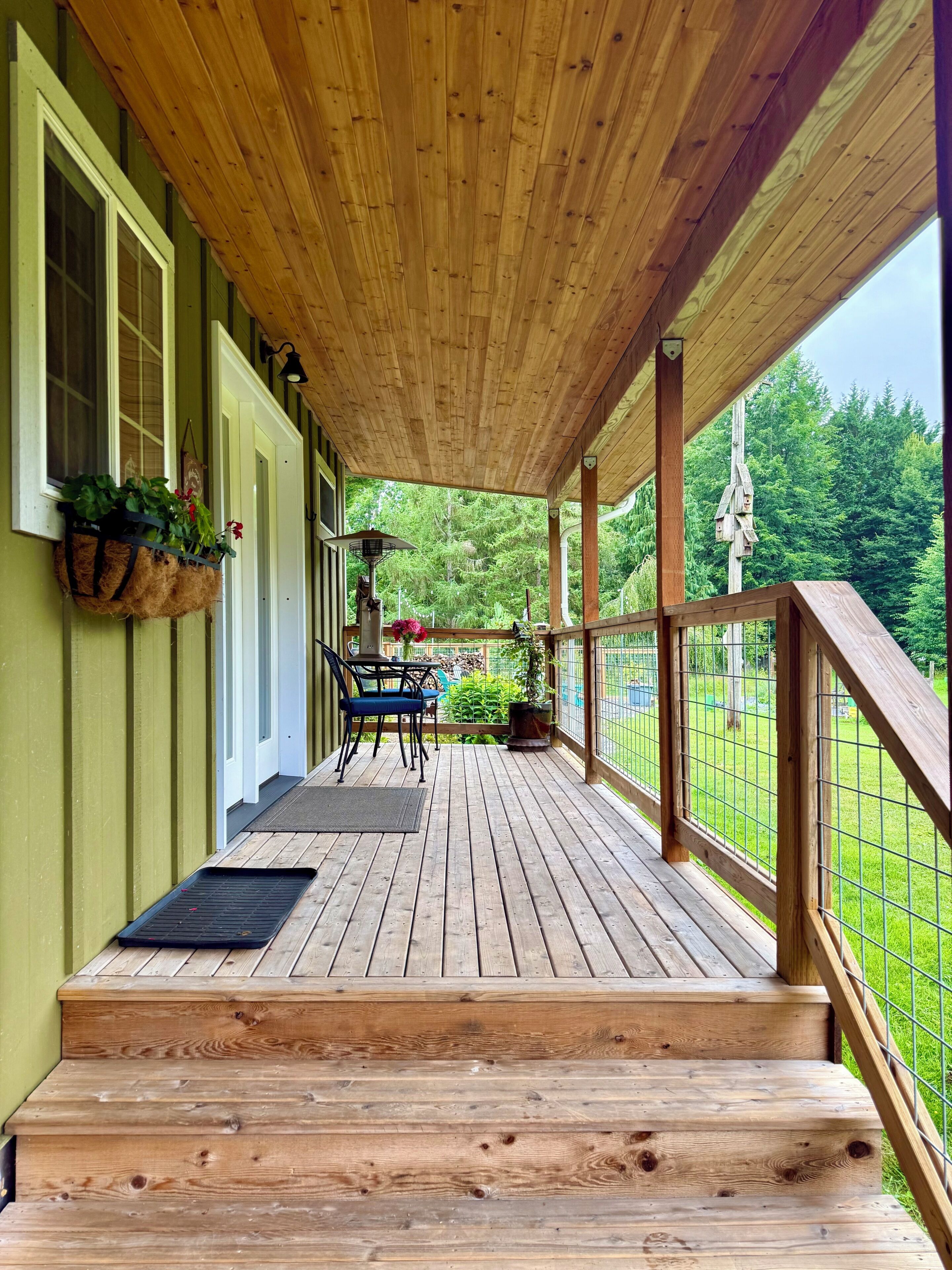 A wooden deck with a railing, a table with chairs, and hanging flower baskets.