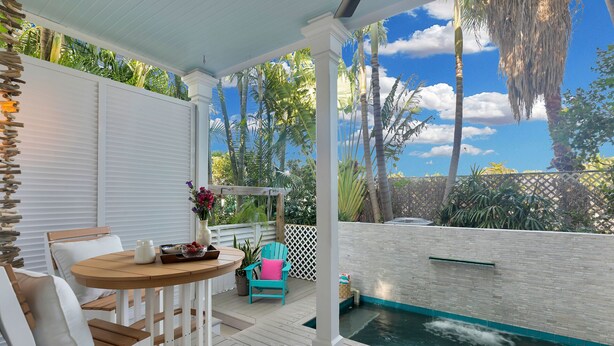Un patio cubierto con piscina, mobiliario de madera y vistas a palmeras y un cielo despejado.