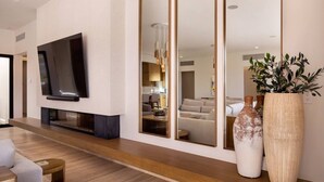A modern living room with a flat-screen TV mounted on the wall, a wooden console table, and two large vases on a console table. - 4BR Ocean/Golf View • Pool & Transfers (Cabo San Lucas)
