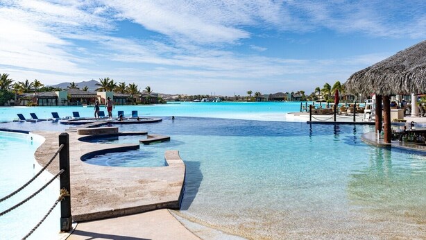A resort pool area with clear water, lounge chairs, and a thatched-roof structure. - 4BR Ocean/Golf View • Pool & Transfers (Cabo San Lucas)