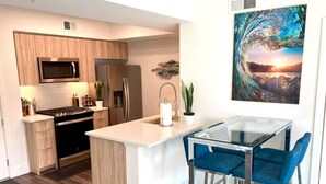 Een moderne keuken met een centraal eiland, roestvrijstalen apparatuur en een glazen eettafel met blauwe stoelen.