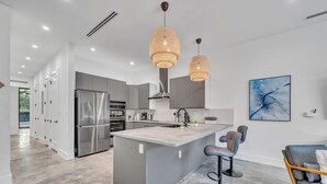 Une cuisine moderne dotée d’un îlot central, d’appareils électroménagers en acier inoxydable et de luminaires suspendus.