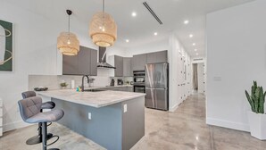 A modern kitchen with a central island, bar stools, stainless steel appliances, and pendant lighting.