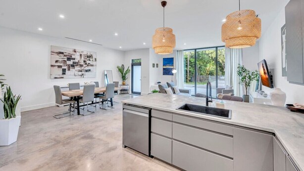 A modern kitchen with a large island, pendant lights, and a dining area with a table and chairs.