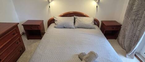 Una cama bien hecha con estructura de madera, dos mesitas de noche y dos lámparas de pared.