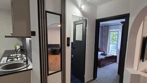 A modern kitchen with a built-in stove and sink, leading to a bedroom with a bed and a window. - Oradea Gateway | 3BR by River | Quick Airport Exit (Oradea)