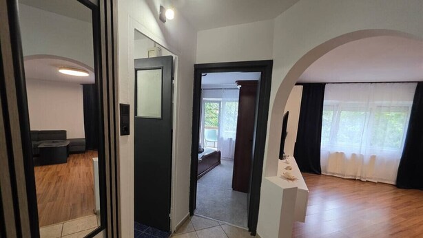 A spacious room with a wooden floor, a white wall, and a door leading to another room. - Oradea Gateway | 3BR by River | Quick Airport Exit (Oradea)
