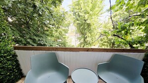 An outdoor seating area with two chairs and a small table, surrounded by greenery and a white wall. - Oradea Gateway | 3BR by River | Quick Airport Exit (Oradea)