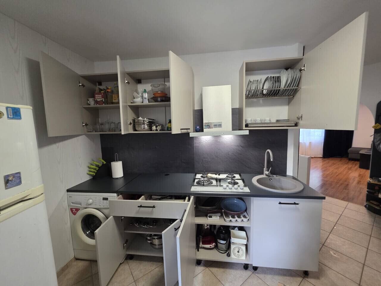 Cuina compacta amb rentadora, un rentabolses, un vàter i una placa de cocció.