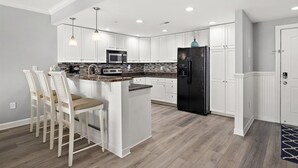 Una cucina moderna con mobili bianchi, un frigorifero nero, un forno a microonde e un'area pranzo con sgabelli da bar.