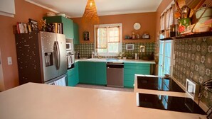 Una cocina con gabinetes verde azulado, una encimera blanca, una lámpara colgante y una ventana con cortinas.