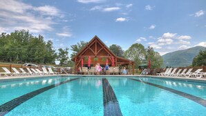 A swimming pool with a wooden pavilion in the center, surrounded by lounge chairs and umbrellas. - Smoky Views & Game 4 BR Cabin w Hot Tub Near Wears Valley! (Sevierville)