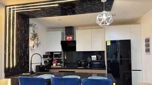 Ett modernt kök med svarta skåp, ett svart kylskåp och en matplats med blå stolar.