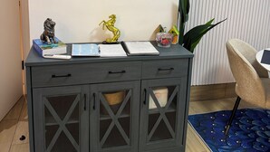 Ett modernt rum med ett grått konsolbord, en rund spegel, en inramad tavla med ett tigermotiv och en liten hundfigur.