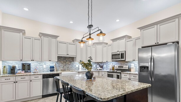 A modern kitchen with white cabinetry, a granite island, stainless steel appliances, and a hanging light fixture. - The Main Stay - Steps from Ohio River, Shopping, & Dining on Main St (Madison)
