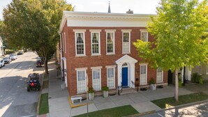 A two-story brick building with a blue door and white trim, located on a tree-lined street. - The Main Stay - Steps from Ohio River, Shopping, & Dining on Main St (Madison)