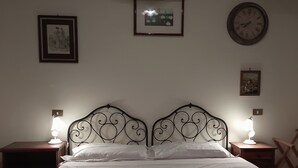 Ein Bett mit Metallkopfteil, zwei Nachttische mit Lampen und gerahmte Bilder an der Wand.