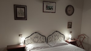 Ein Schlafzimmer mit einem Bett, zwei Nachttischen, einer Wanduhr und gerahmten Bildern.