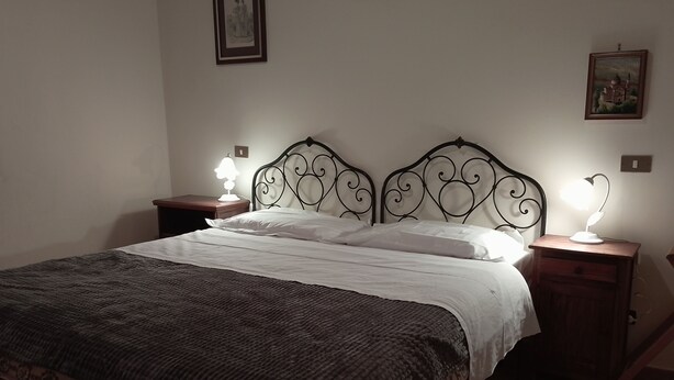 Ein ordentlich bezogenes Bett mit einer dunkel gemusterten Tagesdecke, zwei Nachttische mit Lampen und zwei gerahmte Bilder an der Wand.