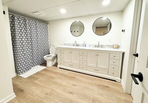A bathroom with a white vanity, two round mirrors, a toilet, and a patterned shower curtain.