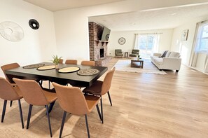 A modern living room with a fireplace, a dining area with a table and chairs, and a seating area with a sofa and armchairs.