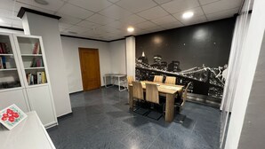 Ein Konferenzraum mit Stadtbild-Wandgemälde, einem Holztisch mit Stühlen, einem Bücherregal und einer Tür.