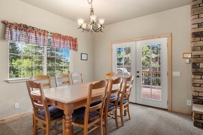 Comedor con mesa y sillas de madera, candelabro y vista por la ventana.