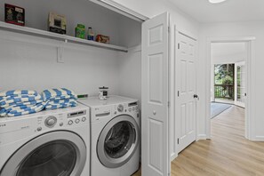 A laundry area with a washing machine and dryer, a shelf with cleaning products, and a door leading to a balcony. - Hawks Nest Dock & Beach Payette Lake McCall, Idaho (McCall)