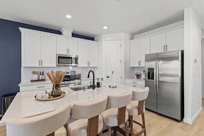 A modern kitchen with white cabinets, stainless steel appliances, and a central island with bar stools.
