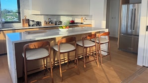 Een moderne keuken met een marmeren aanrecht, houten barstoelen, roestvrijstalen apparatuur en een groot raam.