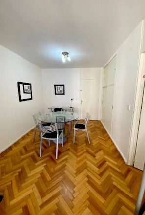 A room with a round glass table surrounded by chairs, a wooden herringbone floor, and white walls. - Beautiful apartment very close to Puerto Madero! Few meters from Florida Street, (BUENOS AIRES)